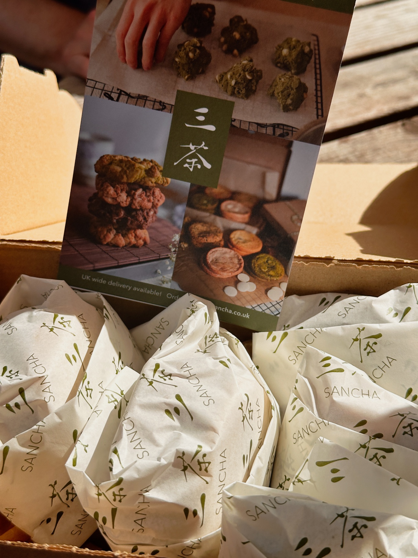 Open Sancha box with cookies individually wrapped in branded paper and a printed brochure standing inside