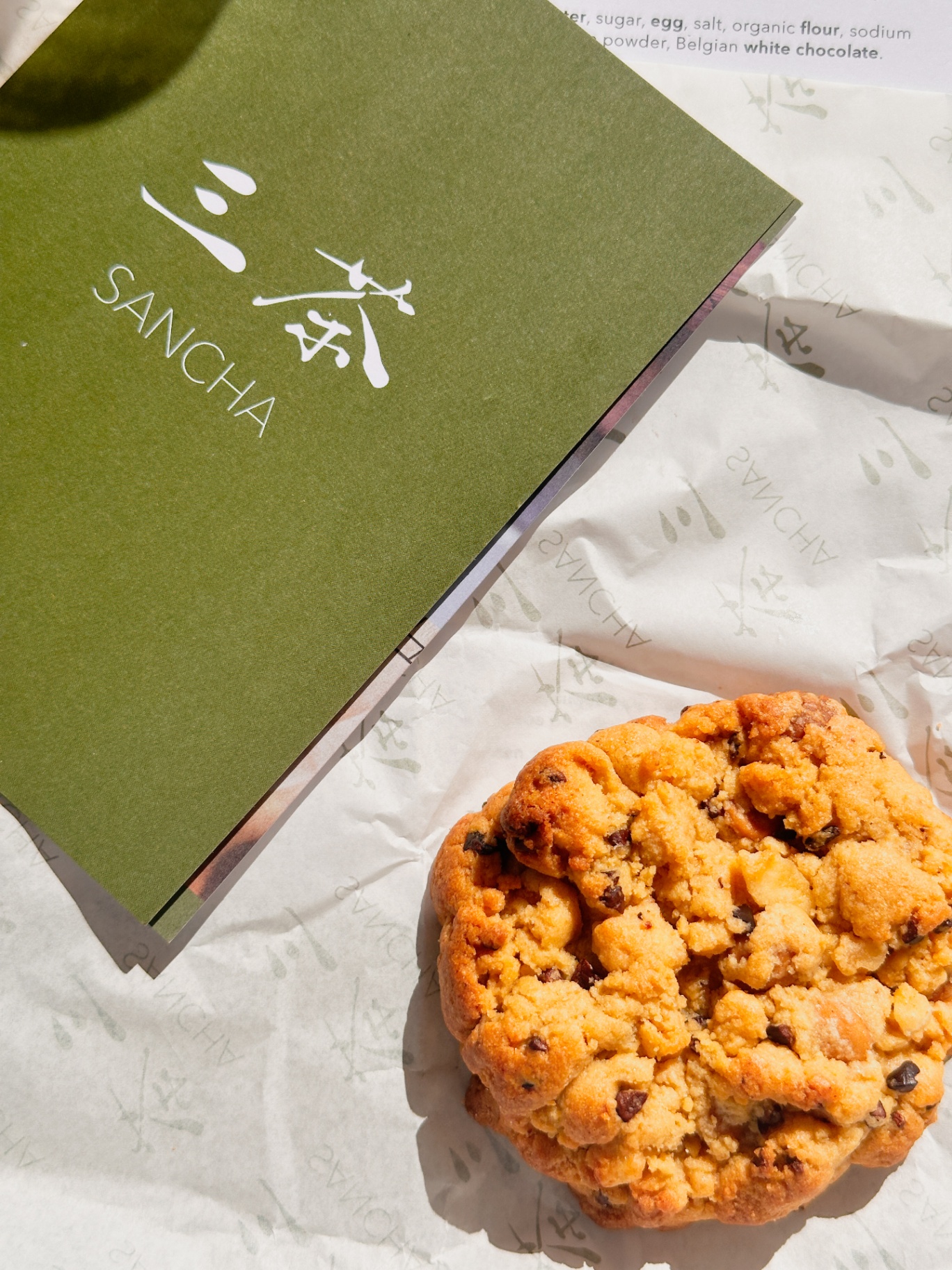 Sancha cookie on a white paper wrapper beside the matcha-green Sancha box, with the ingredient list visible