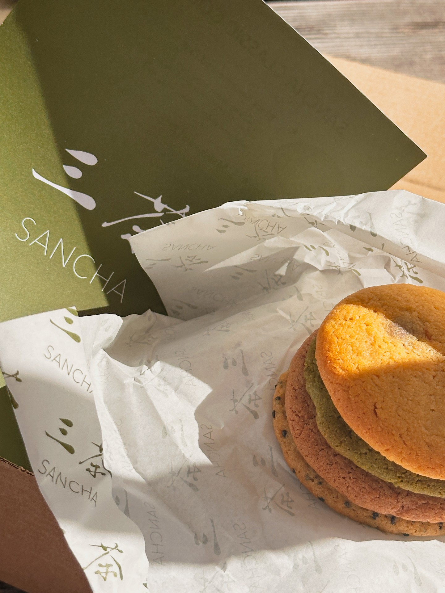 Matcha-green Sancha box with a stack of colourful cookies on patterned paper